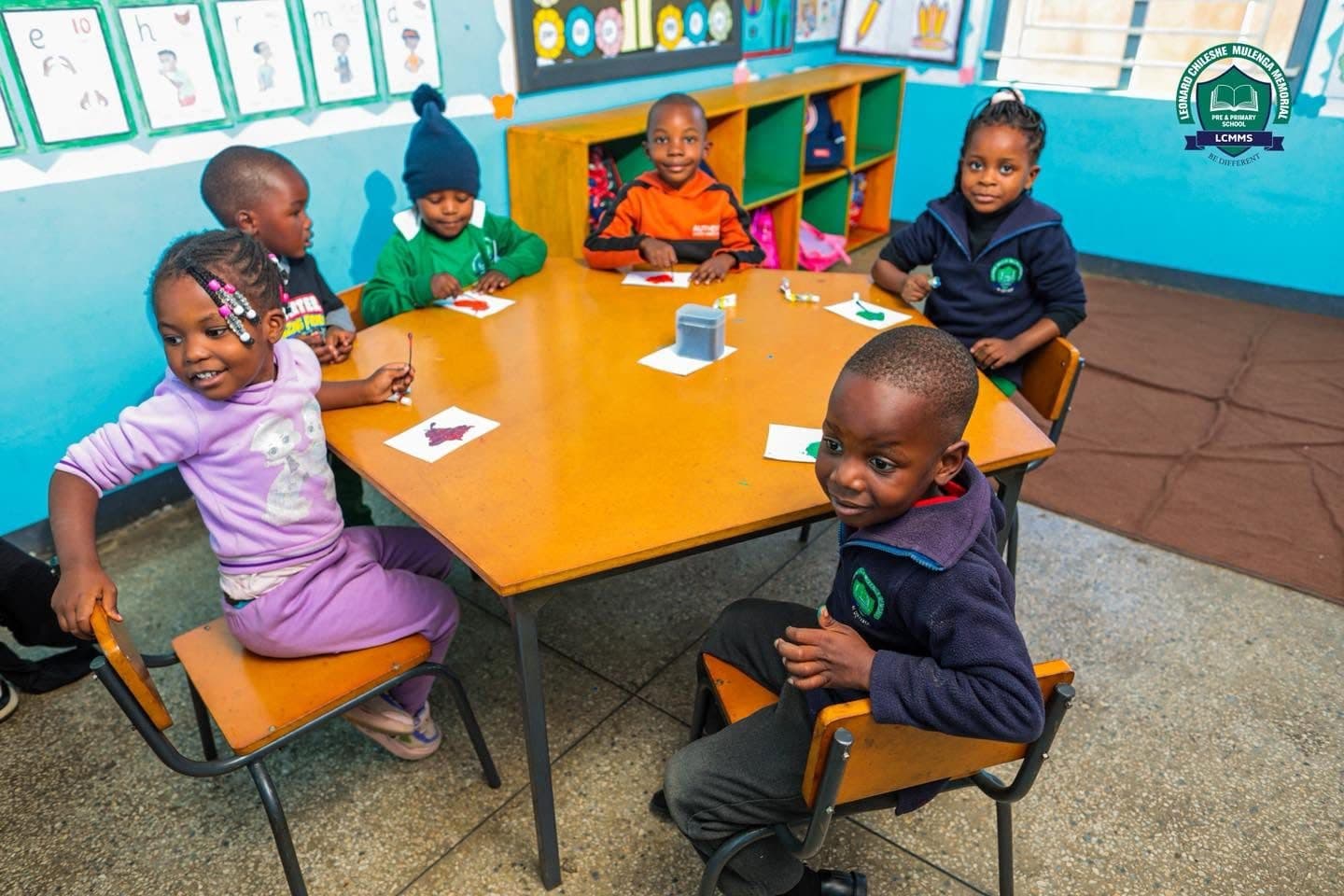 Young pupils painting at a hexagonal table in a bright early-years classroom